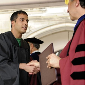 A man in graduation gown shaking hands with another person.
